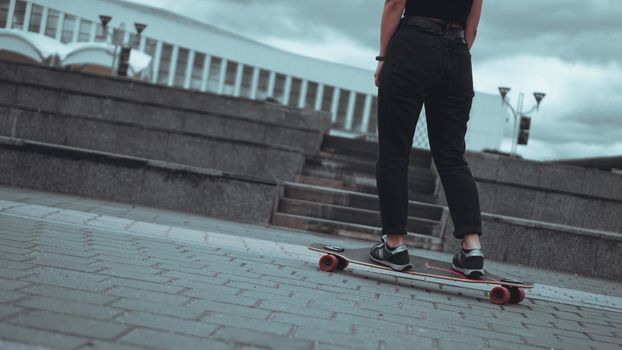 Woman skateboarder legs skateboarding at grey city