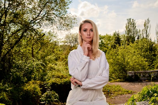 Young blonde woman in white skirt and shirt in the old sunny summer city park. Fashion woman. Young woman's modern portrait.