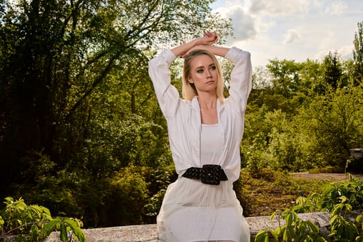 Young blonde woman in white skirt and shirt in the old sunny summer city park. Fashion woman. Young woman's modern portrait.