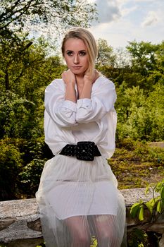 Young blonde woman in white skirt and shirt in the old sunny summer city park. Fashion woman. Young woman's modern portrait.