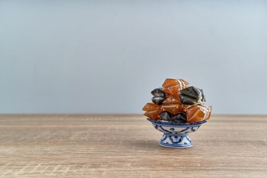 Stack of Thai caramel or Kalamare with sesame on pedestal tray place on wood table with white background and copy space. Sweet and gummy snack of Thai food.