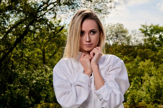 Young blonde woman in white skirt and shirt in the old sunny summer city park. Fashion woman. Young woman's modern portrait.