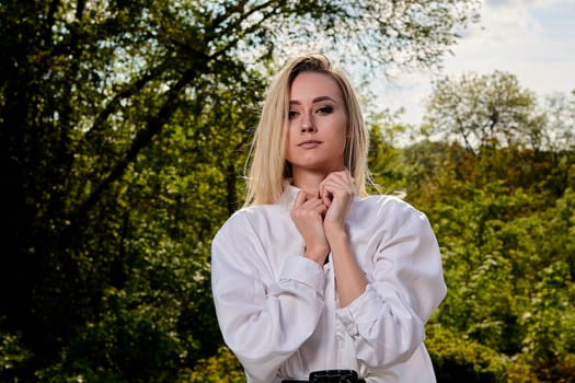 Young blonde woman in white skirt and shirt in the old sunny summer city park. Fashion woman. Young woman's modern portrait.