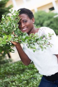 smiling young woman hidden behind foliage looks through.