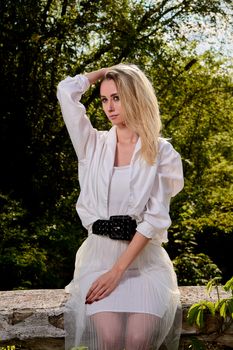 Young blonde woman in white skirt and shirt in the old sunny summer city park. Fashion woman. Young woman's modern portrait.