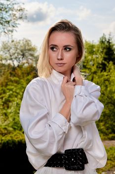 Young blonde woman in white skirt and shirt in the old sunny summer city park. Fashion woman. Young woman's modern portrait.