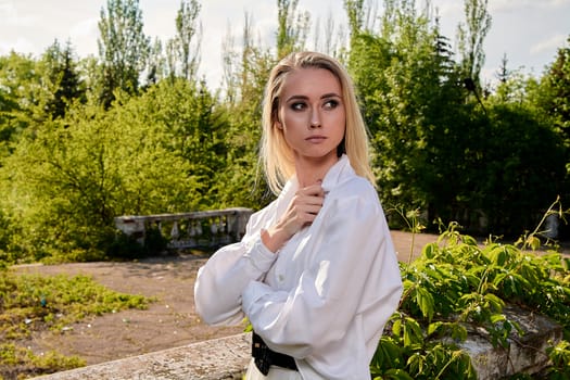 Young blonde woman in white skirt and shirt in the old sunny summer city park. Fashion woman. Young woman's modern portrait.