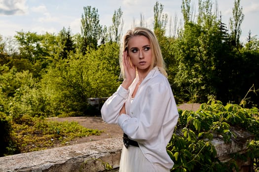 Young blonde woman in white skirt and shirt in the old sunny summer city park. Fashion woman. Young woman's modern portrait.