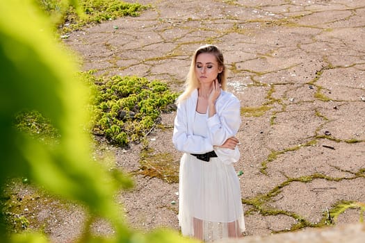 Young blonde woman in white skirt and shirt in the old sunny summer city park. Fashion woman. Young woman's modern portrait.