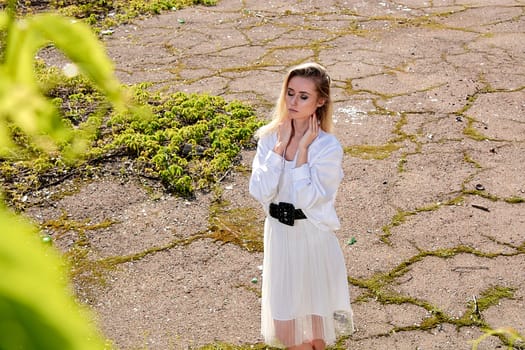 Young blonde woman in white skirt and shirt in the old sunny summer city park. Fashion woman. Young woman's modern portrait.