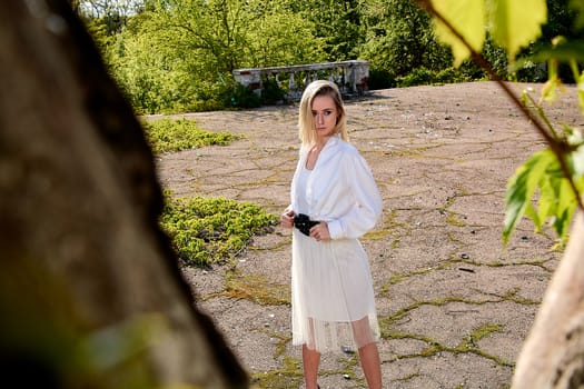 Young blonde woman in white skirt and shirt in the old sunny summer city park. Fashion woman. Young woman's modern portrait.