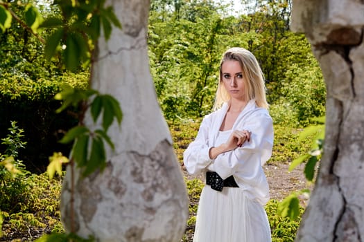 Young blonde woman in white skirt and shirt in the old sunny summer city park. Fashion woman. Young woman's modern portrait.