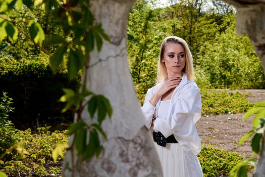 Young blonde woman in white skirt and shirt in the old sunny summer city park. Fashion woman. Young woman's modern portrait.