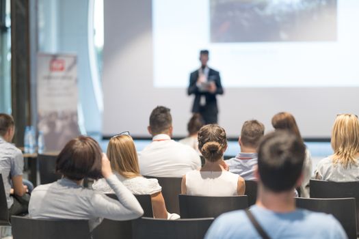 Male speaker giving a talk in conference hall at business event. Audience at the conference hall. Business and Entrepreneurship concept. Focus on unrecognizable people in audience.