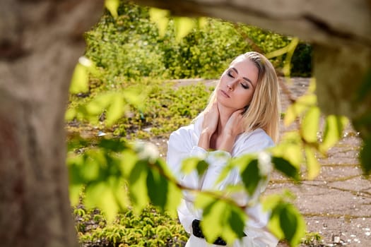 Young blonde woman in white skirt and shirt in the old sunny summer city park. Fashion woman. Young woman's modern portrait.