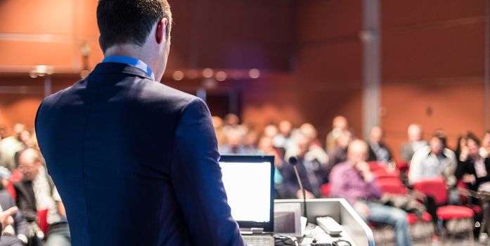 Speaker giving a talk on corporate business conference. Unrecognizable people in audience at conference hall. Business and Entrepreneurship event.