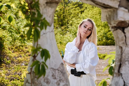 Young blonde woman in white skirt and shirt in the old sunny summer city park. Fashion woman. Young woman's modern portrait.