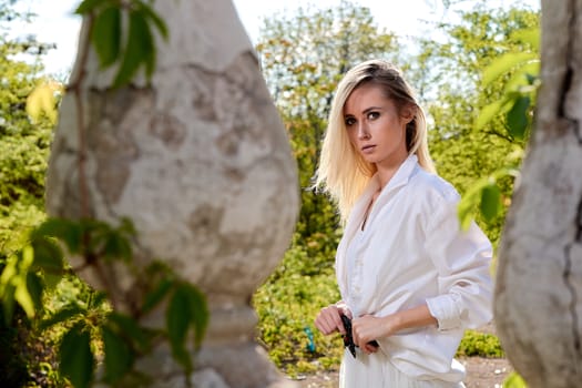 Young blonde woman in white skirt and shirt in the old sunny summer city park. Fashion woman. Young woman's modern portrait.