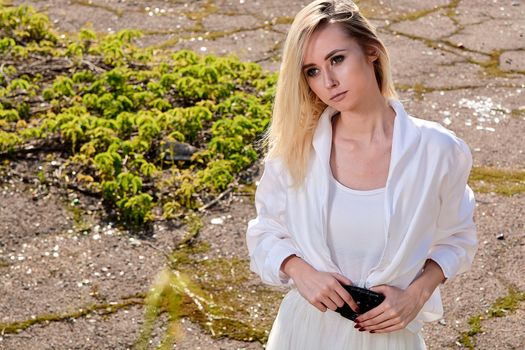 Young blonde woman in white skirt and shirt in the old sunny summer city park. Fashion woman. Young woman's modern portrait.