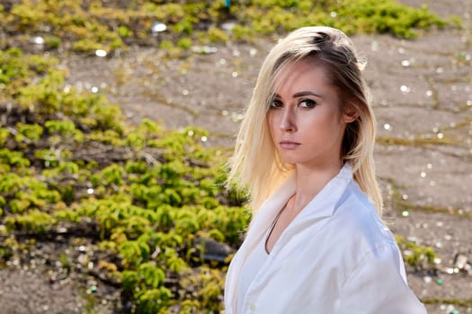 Young blonde woman in white skirt and shirt in the old sunny summer city park. Fashion woman. Young woman's modern portrait.