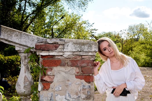 Young blonde woman in white skirt and shirt in the old sunny summer city park. Fashion woman. Young woman's modern portrait.