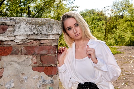 Young blonde woman in white skirt and shirt in the old sunny summer city park. Fashion woman. Young woman's modern portrait.