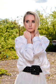 Young blonde woman in white skirt and shirt in the old sunny summer city park. Fashion woman. Young woman's modern portrait.