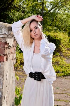 Young blonde woman in white skirt and shirt in the old sunny summer city park. Fashion woman. Young woman's modern portrait.