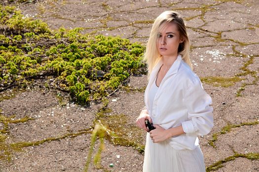 Young blonde woman in white skirt and shirt in the old sunny summer city park. Fashion woman. Young woman's modern portrait.