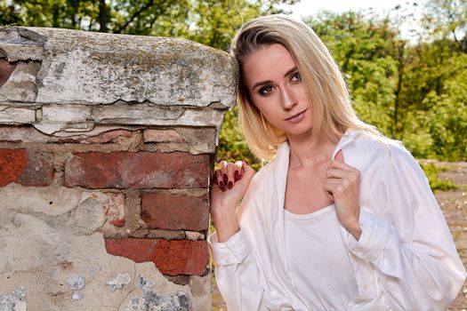 Young blonde woman in white skirt and shirt in the old sunny summer city park. Fashion woman. Young woman's modern portrait.