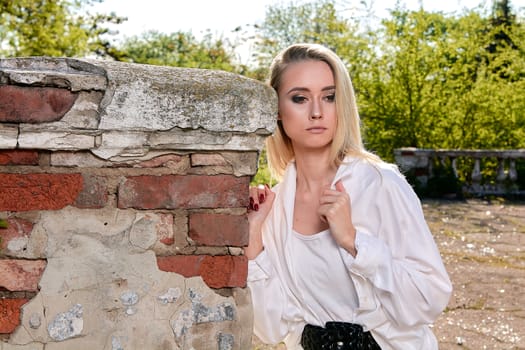 Young blonde woman in white skirt and shirt in the old sunny summer city park. Fashion woman. Young woman's modern portrait.