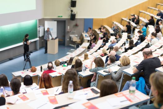 Speaker giving a talk in conference hall at business event. Audience at the conference hall. Business and Entrepreneurship concept. Focus on unrecognizable people in audience.