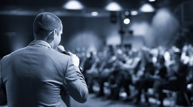 Speaker giving a talk on corporate business conference. Unrecognizable people in audience at conference hall. Business and Entrepreneurship event.