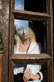 Young blonde woman in white skirt and shirt stands in the old wooden doorway. The old wooden door. Fashion woman. Young woman modern portrait.