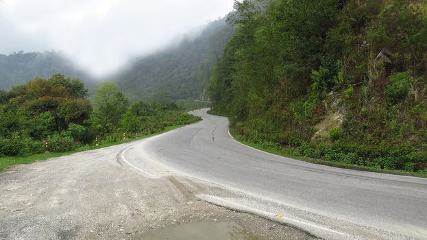 A beautiful curving highway in the Himalayan mountains of Bhutan with lowering clouds.                               