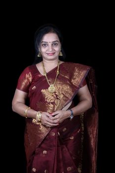 A traditional middle-aged Indian woman in a dark crimson colored Sari, on black studio background