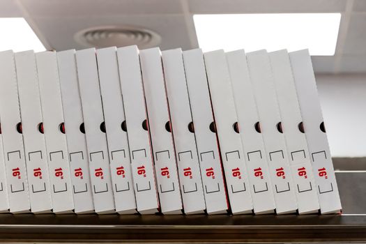 A large stack of white pizza boxes with red numbers diaimeter 16
