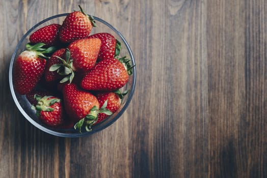 Heap of fresh strawberries in bowl on rustic wooden background, healthy sweet food, vitamins and fruity concept. Top view point, copy space for text