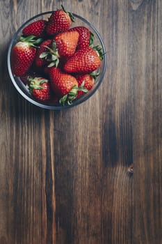 Heap of fresh strawberries in bowl on rustic wooden background, healthy sweet food, vitamins and fruity concept. Vertical photo. Top view point, copy space for text