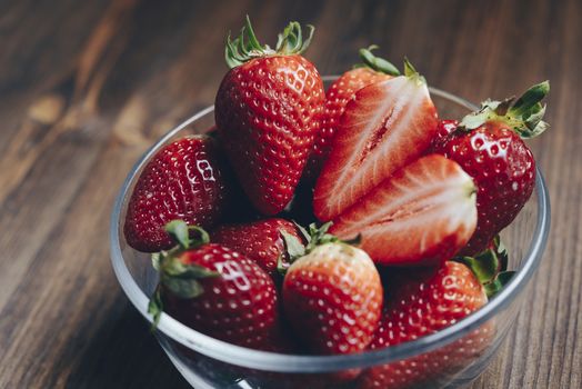 Fresh strawberries in a glass bowl on wooden table in rustic style, healthy sweet food, vitamins and fruity concept