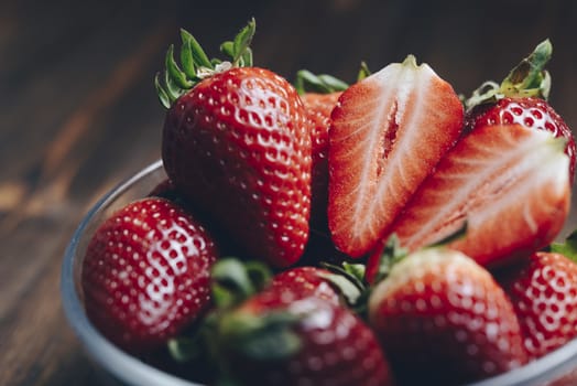 Fresh strawberries in a glass bowl on wooden background in rustic style, healthy sweet food, vitamins and fruity concept. Selective focus