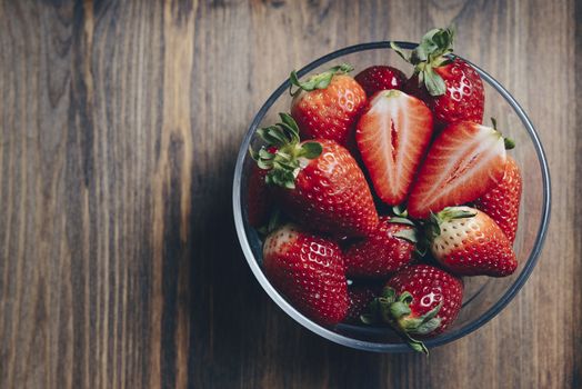 Fresh strawberries in a glass bowl on wooden table in rustic style, healthy sweet food, vitamins and fruity concept. Top view, copy space for text