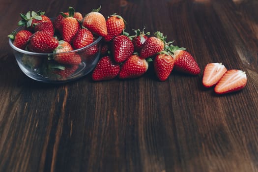 Fresh and juicy strawberries in a glass bowl on wooden background in rustic style, healthy sweet food, vitamins and fruity concept. Copy space for text