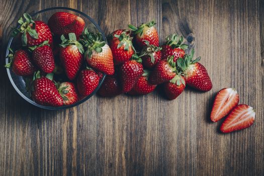 Fresh and juicy strawberries in a glass bowl on wooden table in rustic style, healthy sweet food, vitamins and fruity concept. Top view, copy space for text