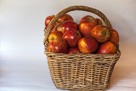 Still life image of a wicker  basket filled with large red Starking apples on a white background.