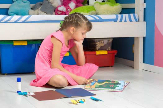 A girl chooses a hand-made article in her book to make it from a colored paper