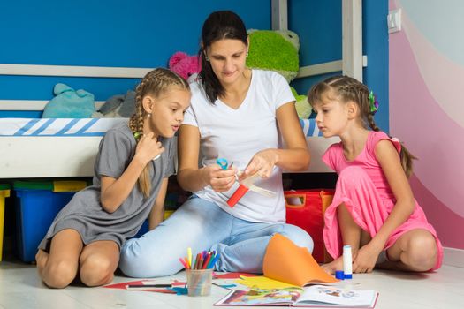 Mom shows daughters how to cut out figures from colored paper