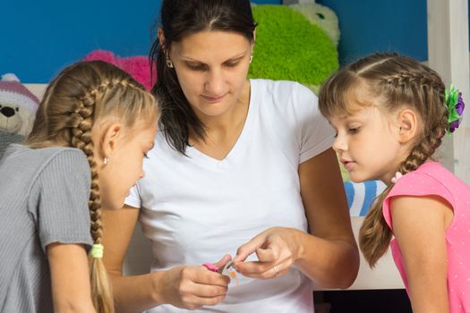 Mom shows daughters how to cut out a hand-made paper from a colored paper