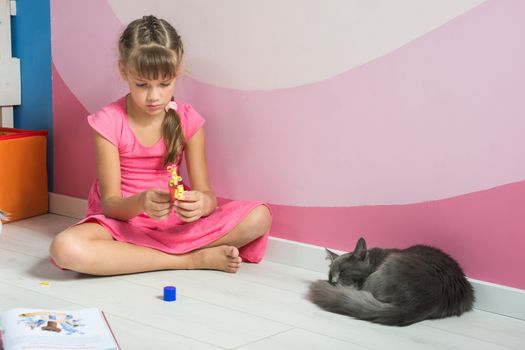 A girl is making figures out of colored paper, a domestic cat is sleeping nearby