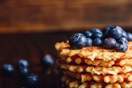 Blueberries on the Top of the Waffles Stack and Other Scattered on Wooden Background. Copy Space on the Left.